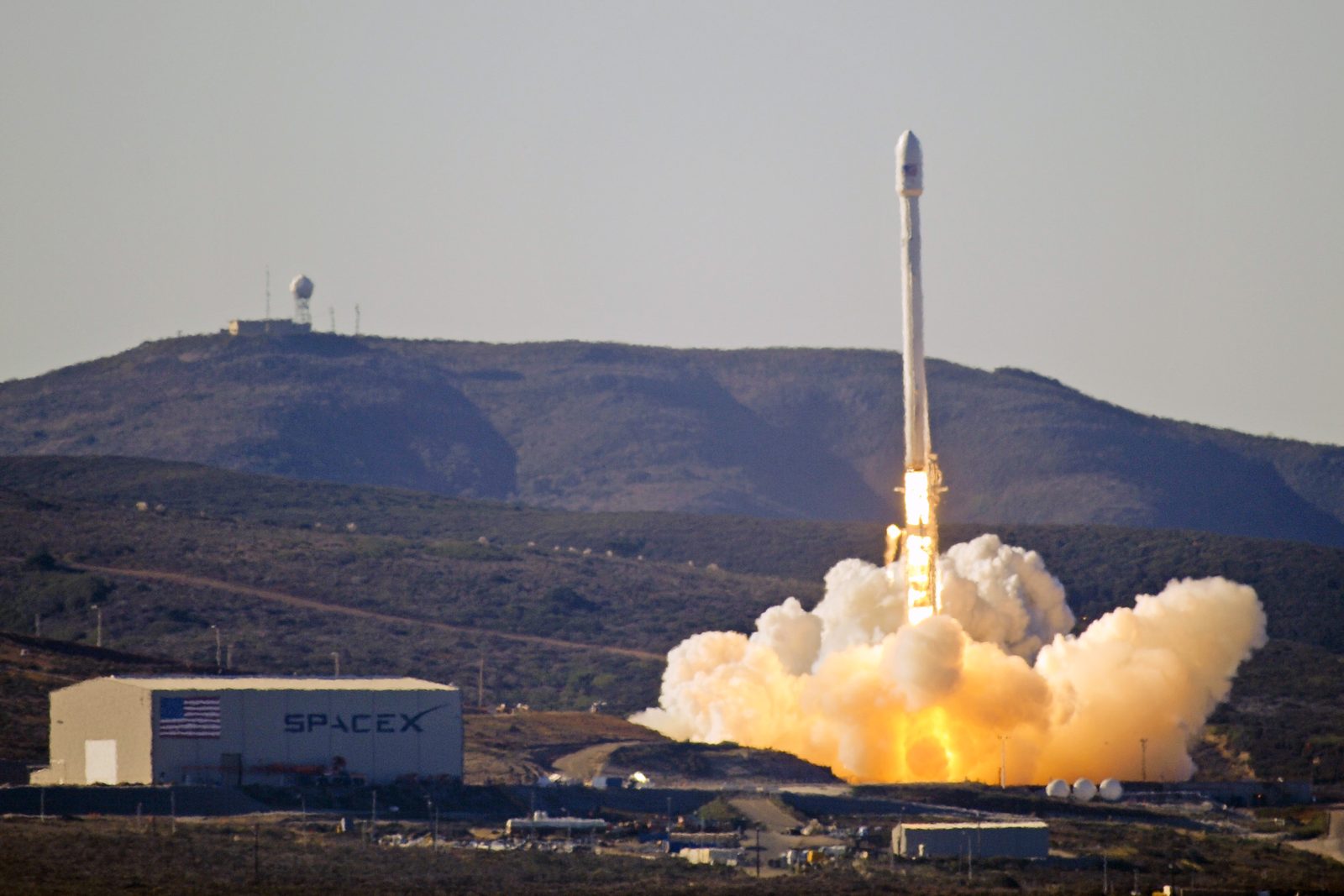 A Falcon 9 rocket lifting off from Vandenberg Space Force Base with a bright orange exhaust plume
