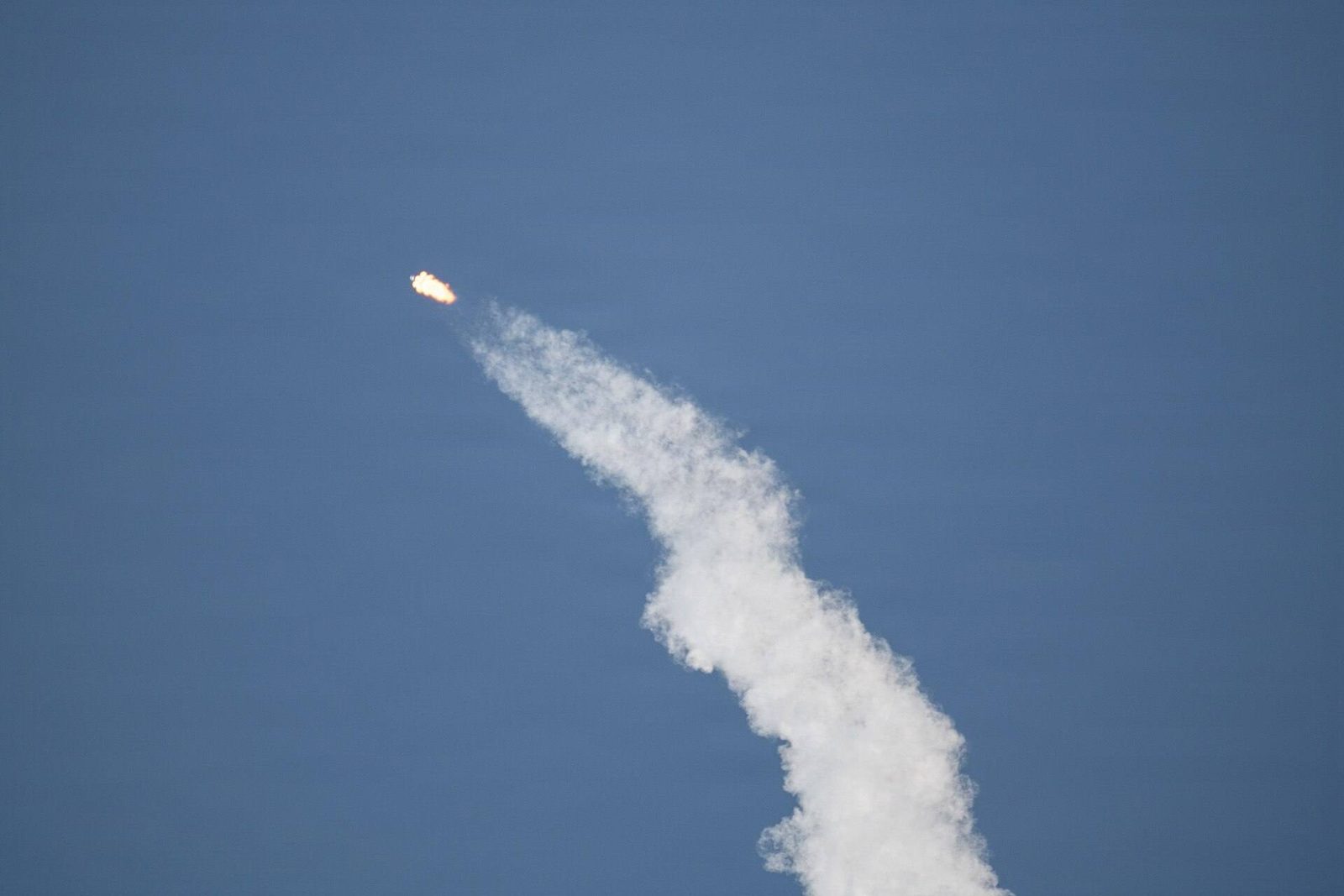 A Falcon 9 rocket climbing through a blue sky with a long white exhaust trail